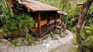 A wooden cabin with a tiled roof, surrounded by lush greenery and a stone pathway leading to a wooden staircase. - Pousada Paraíso do Luz (Imbituba)