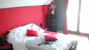 Ein Bett mit roter und weißer Bettwäsche, ein schwarzer Nachttisch und ein roter Sessel.