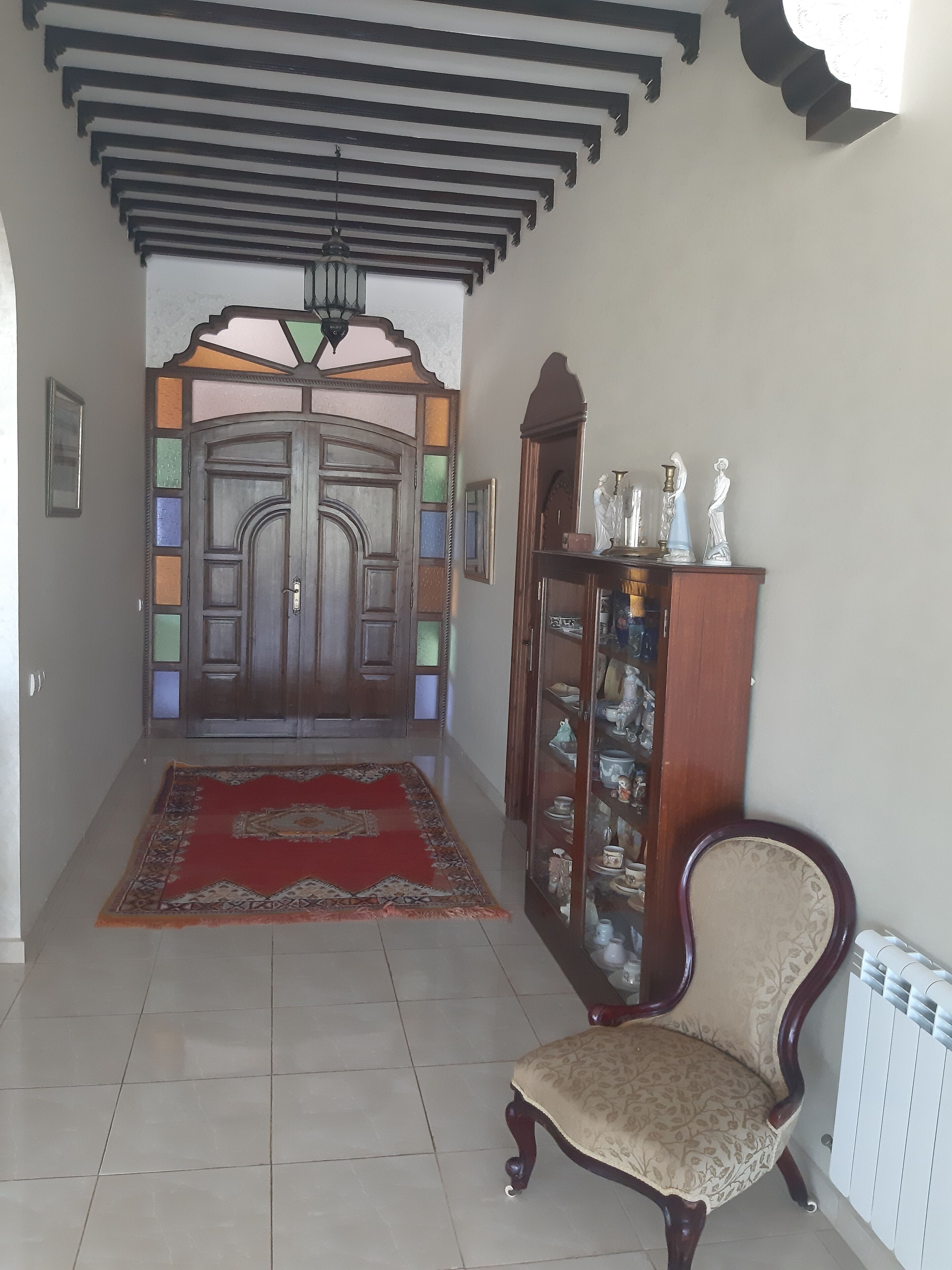 Un pasillo con puerta de madera, alfombra roja, armario de madera con puertas de cristal y una silla.