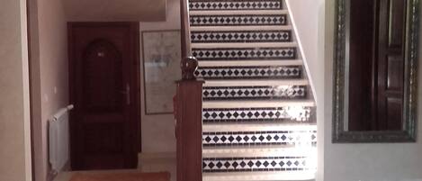 Uma escadaria com azulejos estampados, um gato no chão e um candeeiro pendente tradicional.