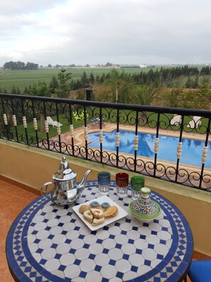 Un balcon donnant sur une piscine et des champs verdoyants.