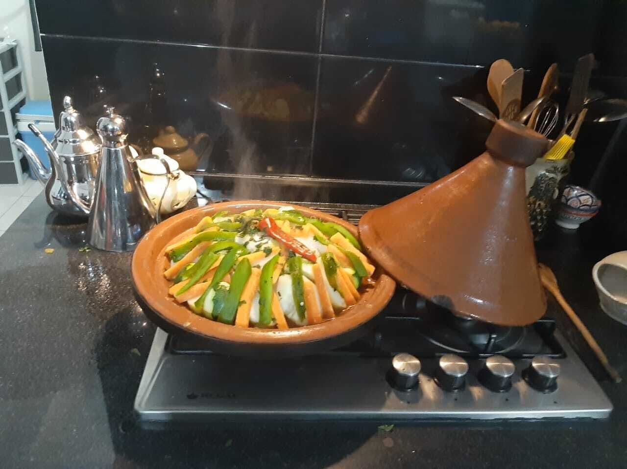 Et køkken med en traditionel lerpotte på komfuret, en gryde med suppe og diverse køkkenredskaber.