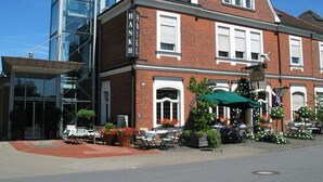 A hotel with a brick facade, large windows, and a covered outdoor seating area with tables and chairs. - Hotel Restaurant Lindenhof (Emsdetten)