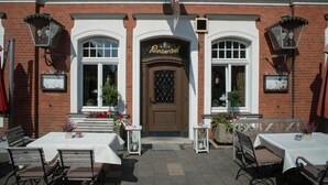 A brick building with a central entrance, two windows on either side, and outdoor seating with tables and chairs. - Hotel Restaurant Lindenhof (Emsdetten)