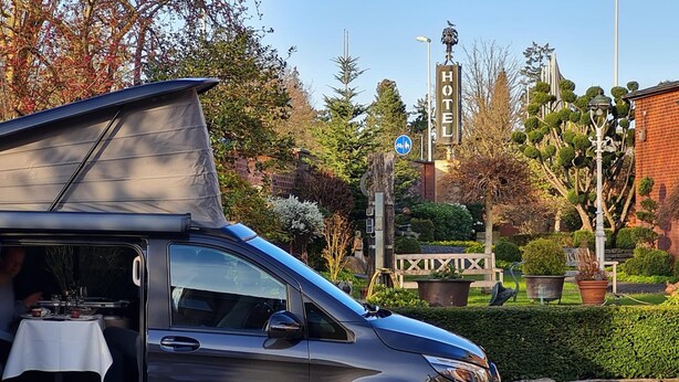 A compact, modern vehicle with a covered cargo area, parked in a well-maintained garden with a 'HOTEL' sign in the background. - Hotel Restaurant Lindenhof (Emsdetten)