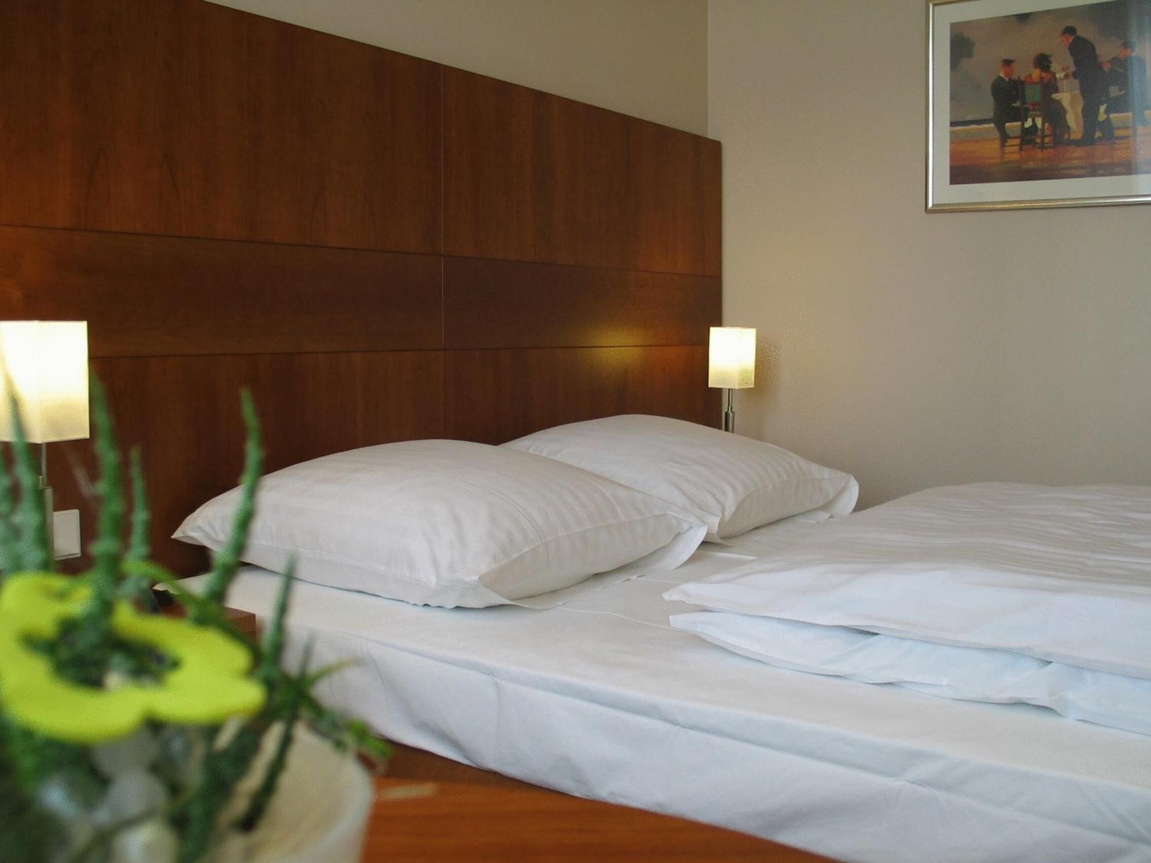 Una habitación de hotel con cabecera de madera, dos camas blancas y un cuadro en la pared.