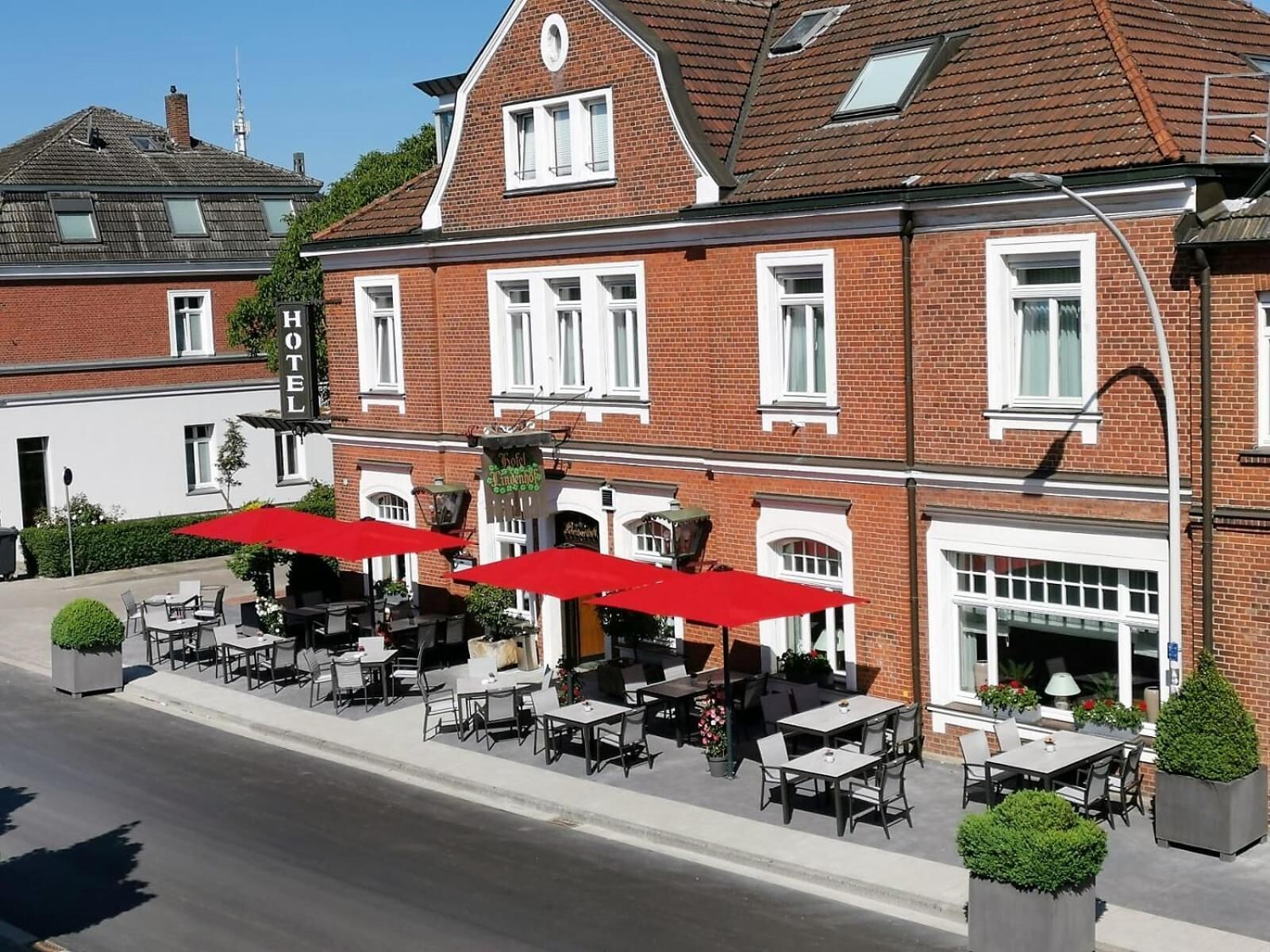A hotel with outdoor seating, red umbrellas, and brick architecture.