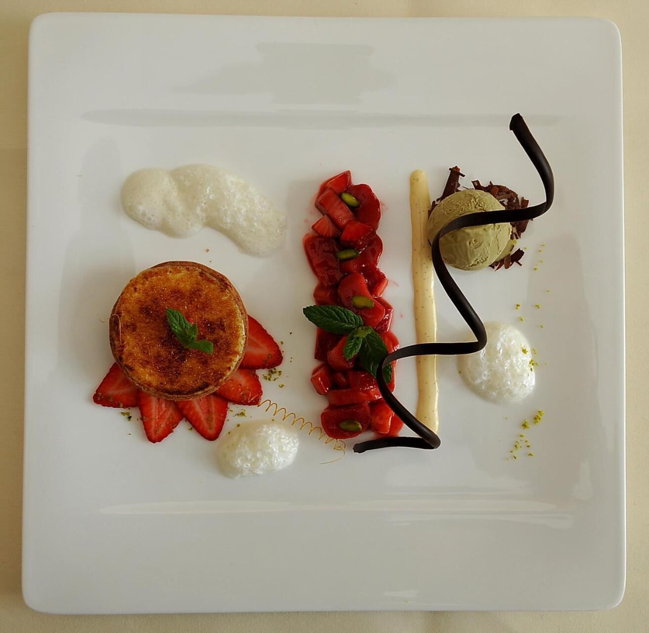 A white plate with a dessert consisting of a round pastry, strawberries, and a chocolate drizzle.