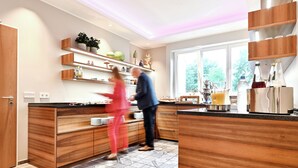 A modern kitchen with wooden cabinets, built-in shelves, and a large window providing natural light. - Hotel Restaurant Lindenhof (Emsdetten)