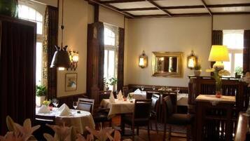 A dining area with tables set for two, wooden beams on the ceiling, and wall-mounted lamps.