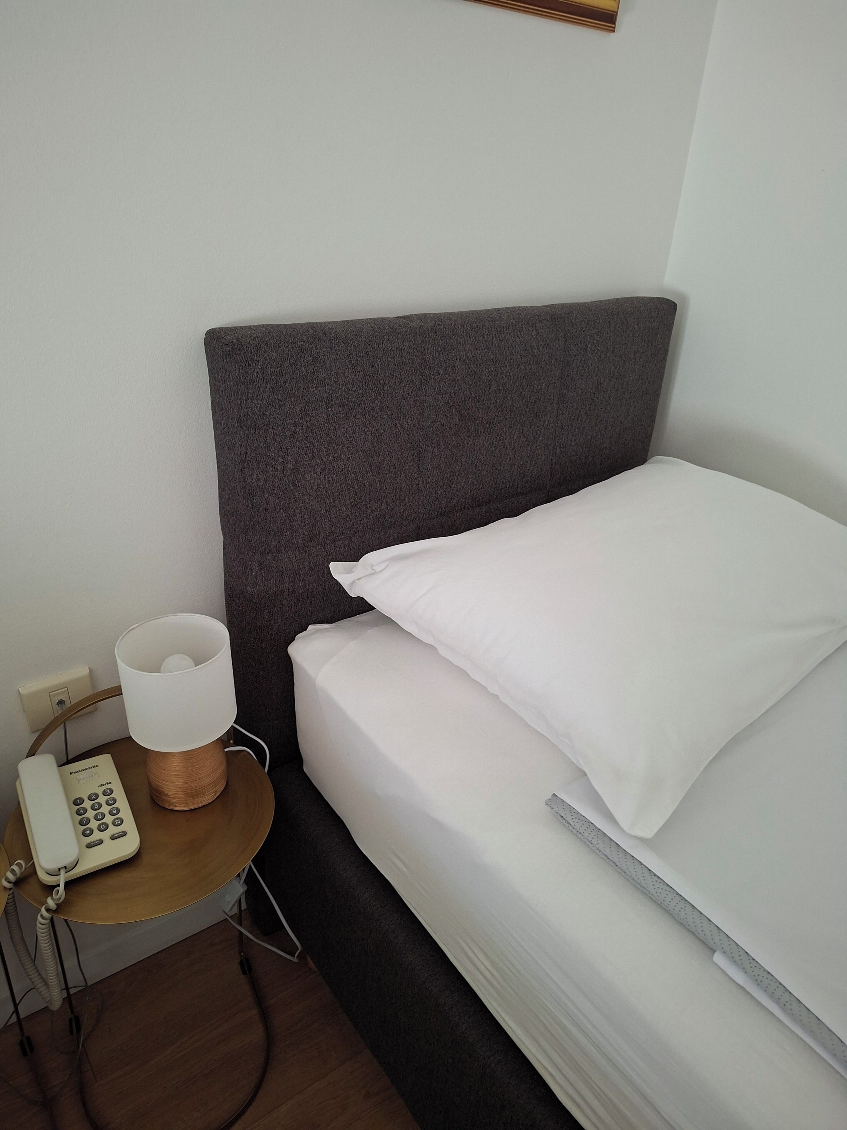 Een hotelkamer met een bed, een bedlampje, een telefoon en een klein tafeltje.