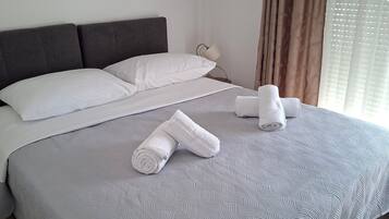 Una cama bien tendida con una colcha estampada, una almohada y dos toallas enrolladas.