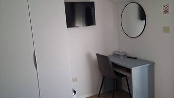 Un dormitorio moderno con cama, escritorio, silla, armario, televisor y espejo.