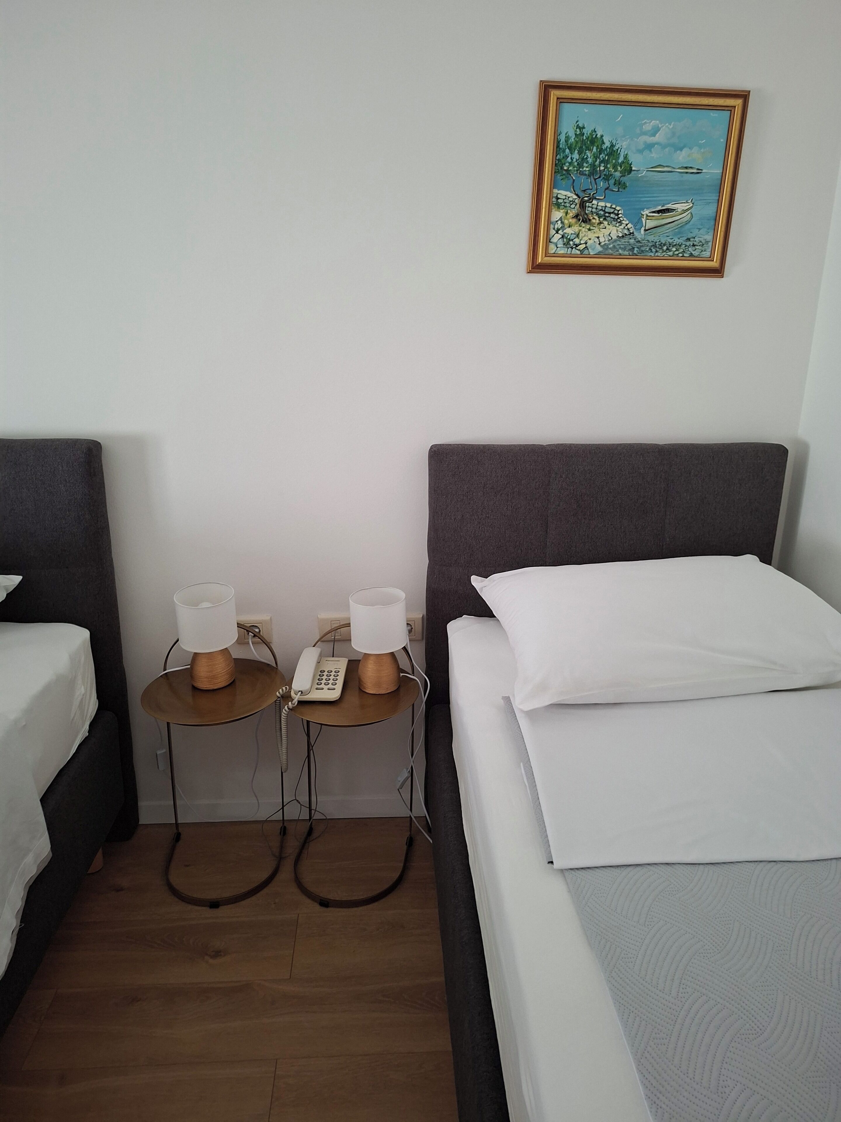 A hotel room with a bed, a bedside table with a lamp, a phone, and a painting on the wall.