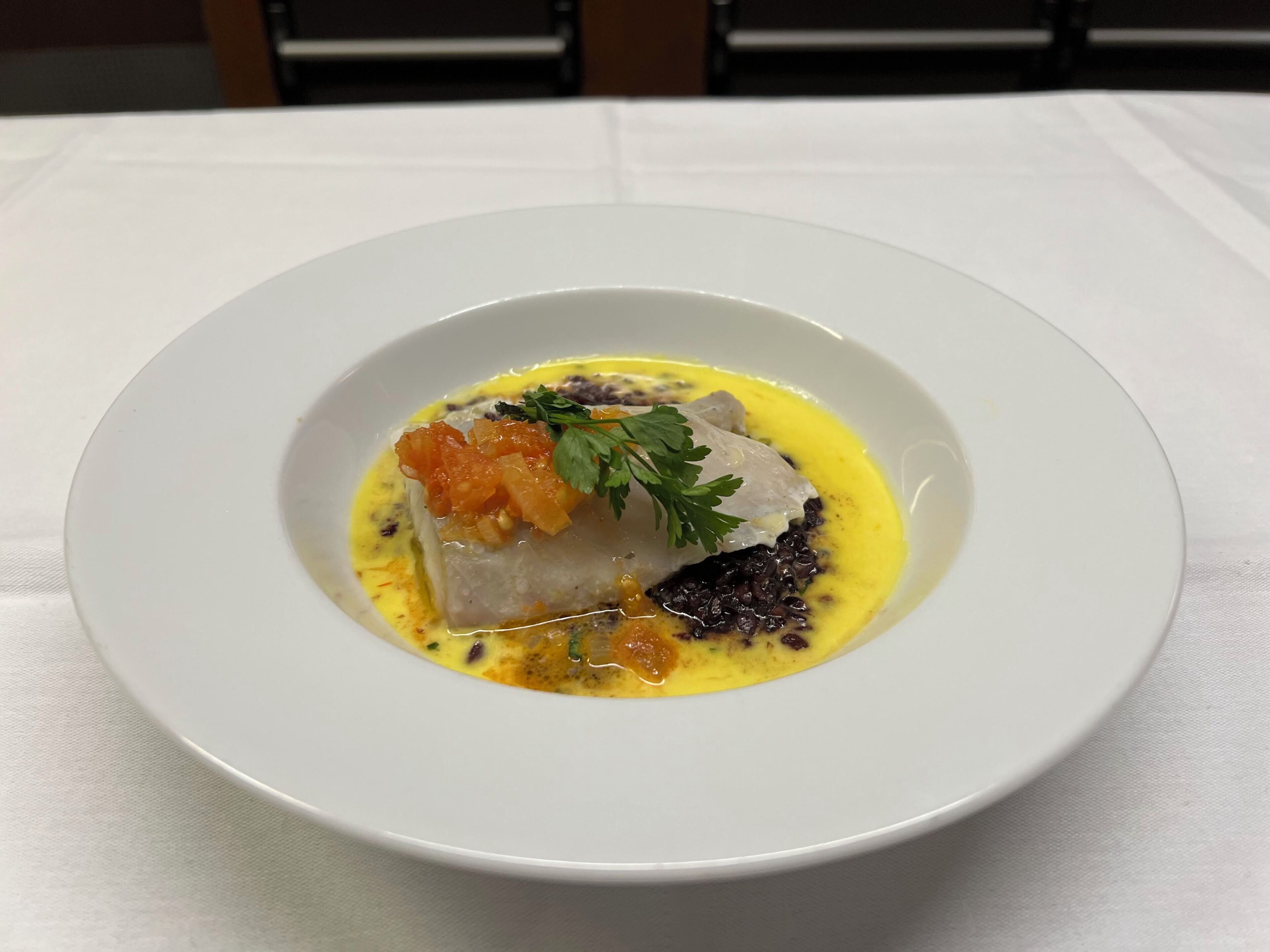 A white plate with a fish dish, a garnish, and a yellow sauce.