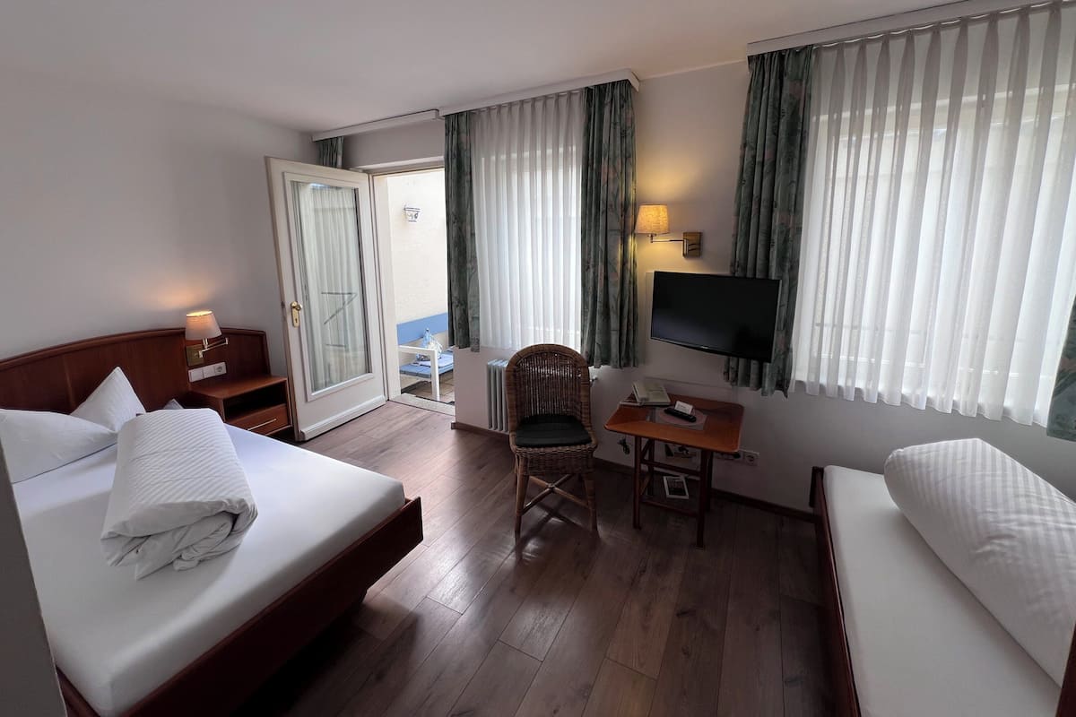 Une chambre d’hôtel comprenant un lit, un bureau avec une chaise, une télévision et une porte coulissante donnant sur un balcon.