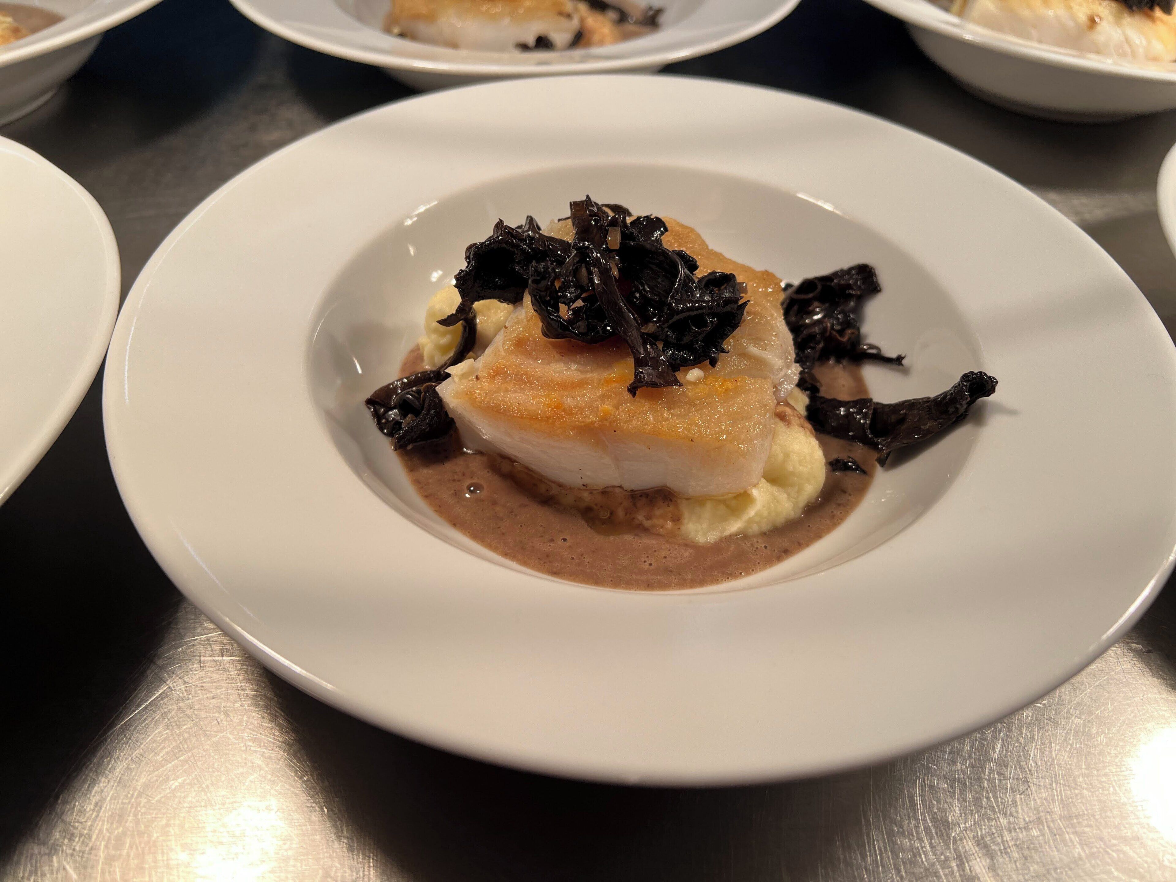 Ein weißer Teller mit Fisch, Kartoffelstampf und brauner Soße.