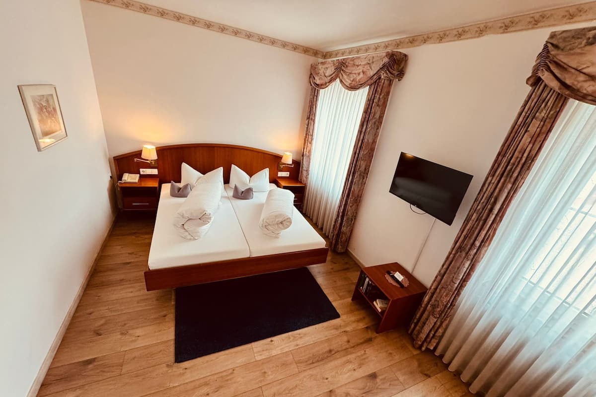 Une chambre d’hôtel avec un lit double, des tables de chevet, une télévision et une fenêtre avec des rideaux.