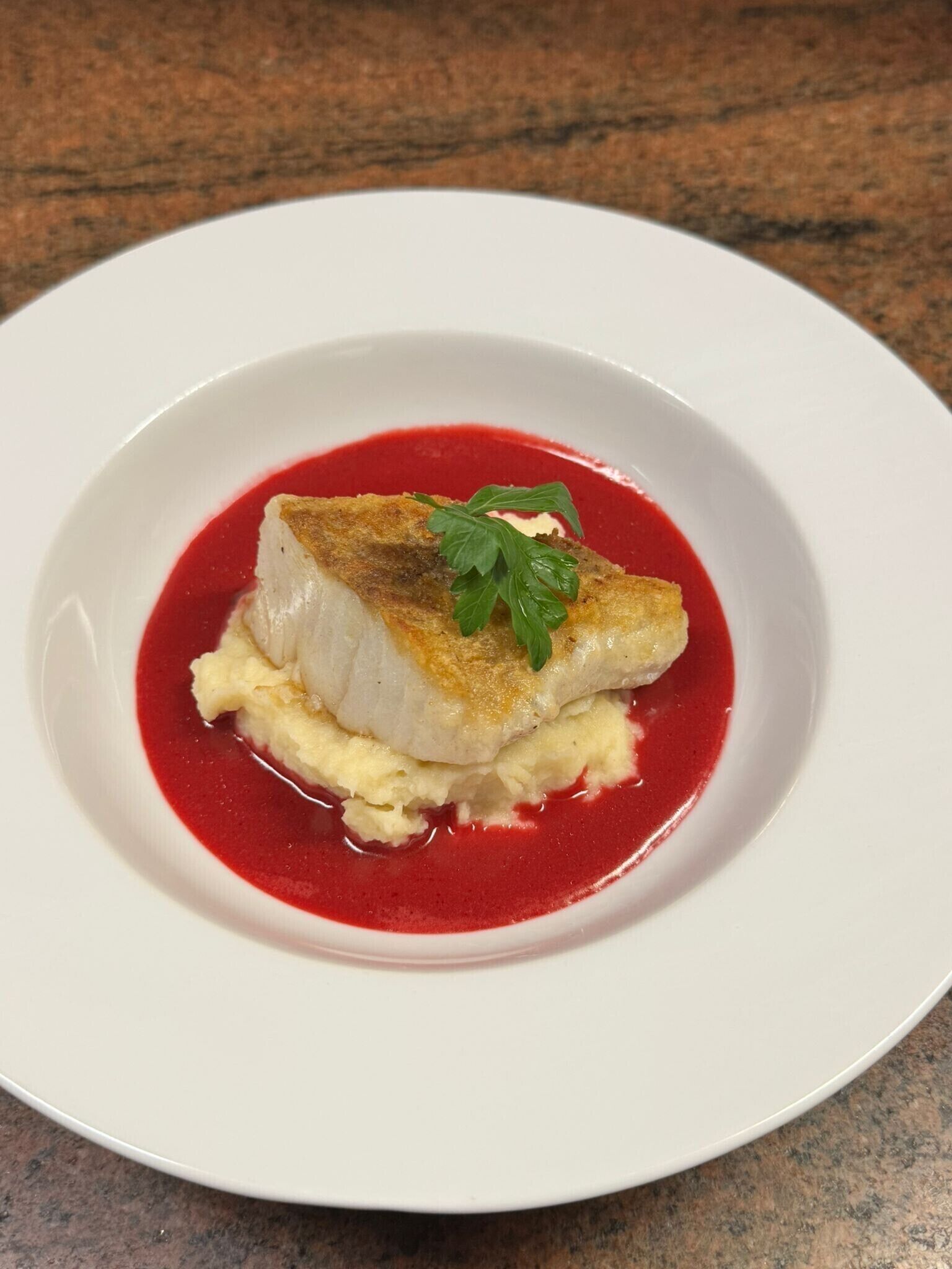 A white plate with a piece of fish, a garnish, and a red sauce.