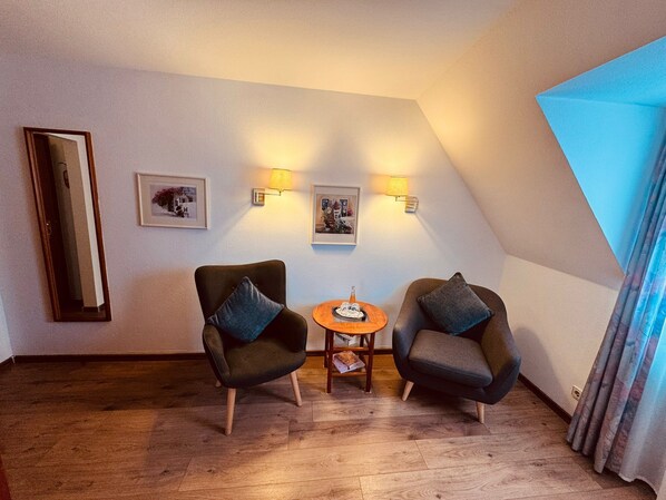 A room with two armchairs, a small table, wall-mounted lamps, framed pictures, and a large window with curtains. - Hotel Restaurant Kaiserstuehler Hof (Breisach)