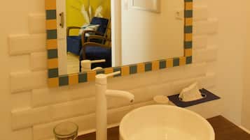 Ein Badezimmer mit einem weißen Waschbecken, einem Spiegel mit kariertem Rahmen, einem Handtuchspender und einer Wandleuchte.