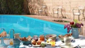 Desayuno junto a la piscina, con una variedad de alimentos y bebidas, como pasteles, frutas y un jarrón de flores.