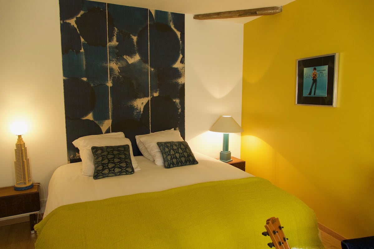 A bedroom with a bed, pillows, a lamp, and a guitar.