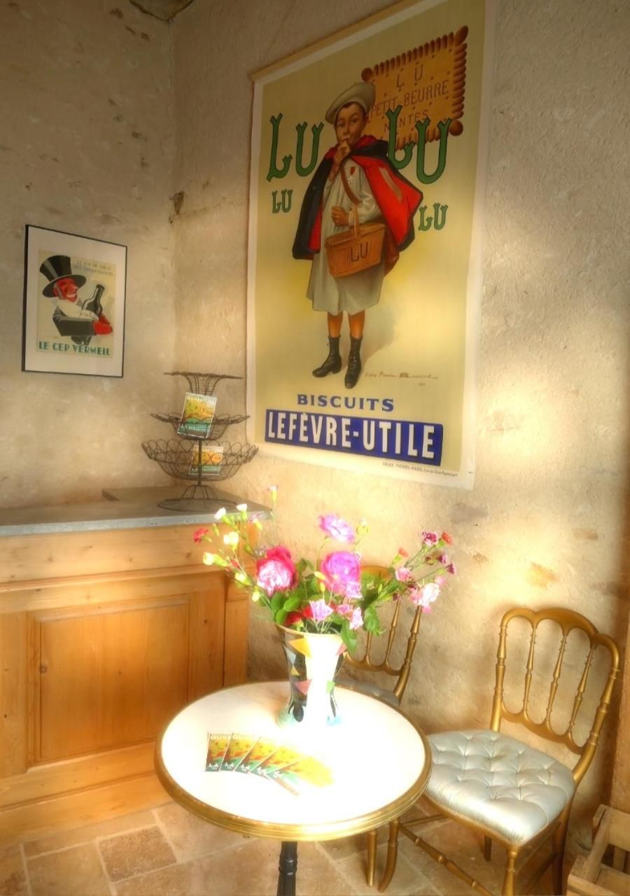 Une affiche ancienne, une petite table avec un vase de fleurs et une chaise dans une pièce aux murs lambrissés.