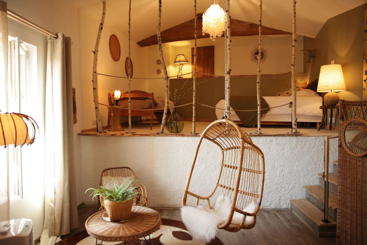 A cozy room with a bed, a hanging chair, a small table with a plant, and a lamp.