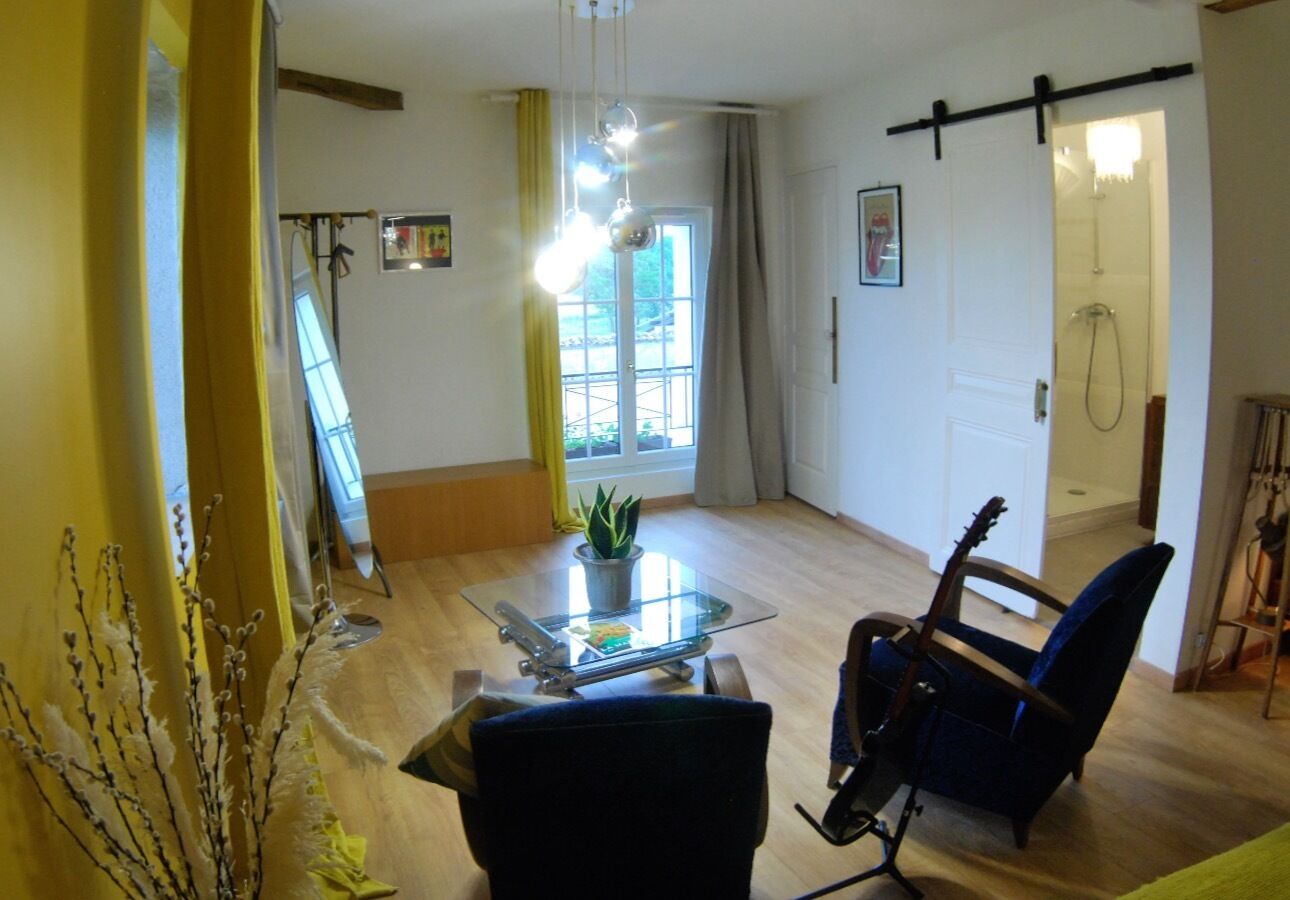 A spacious living room with a glass coffee table, a blue armchair, a guitar, and a potted plant.