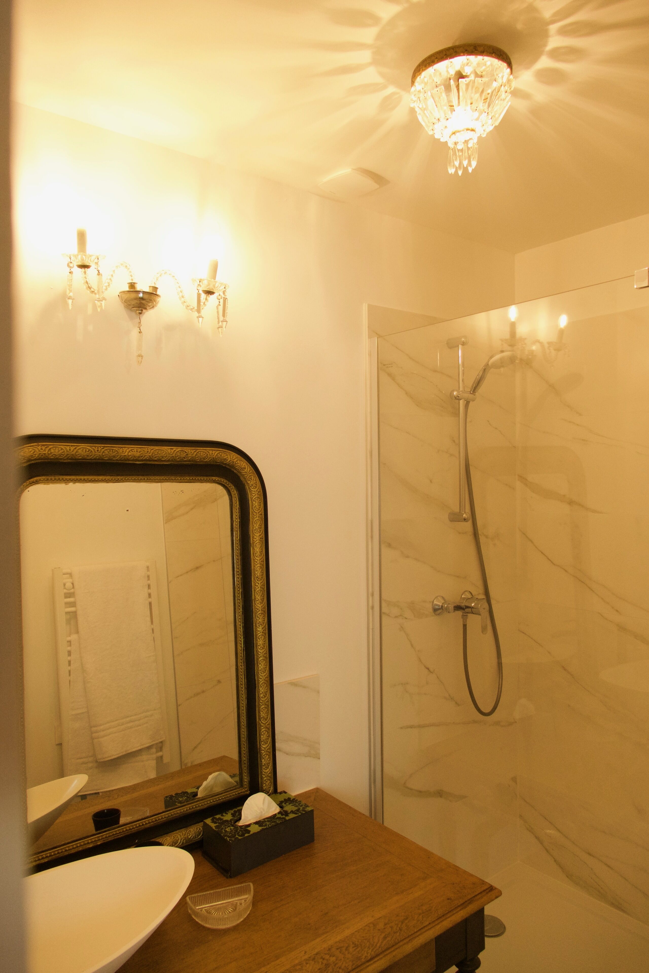A bathroom with a large mirror, a sink, a shower with a glass door, and a chandelier.