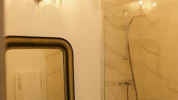 A bathroom with a large mirror, a sink, a shower with a glass door, and a chandelier.