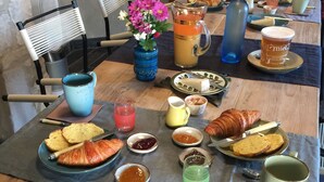 Una mesa de desayuno con cruasanes, pan, mermeladas y una jarra de jugo de naranja.