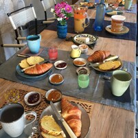 A breakfast table with croissants, bread, jams, and a pitcher of orange juice.