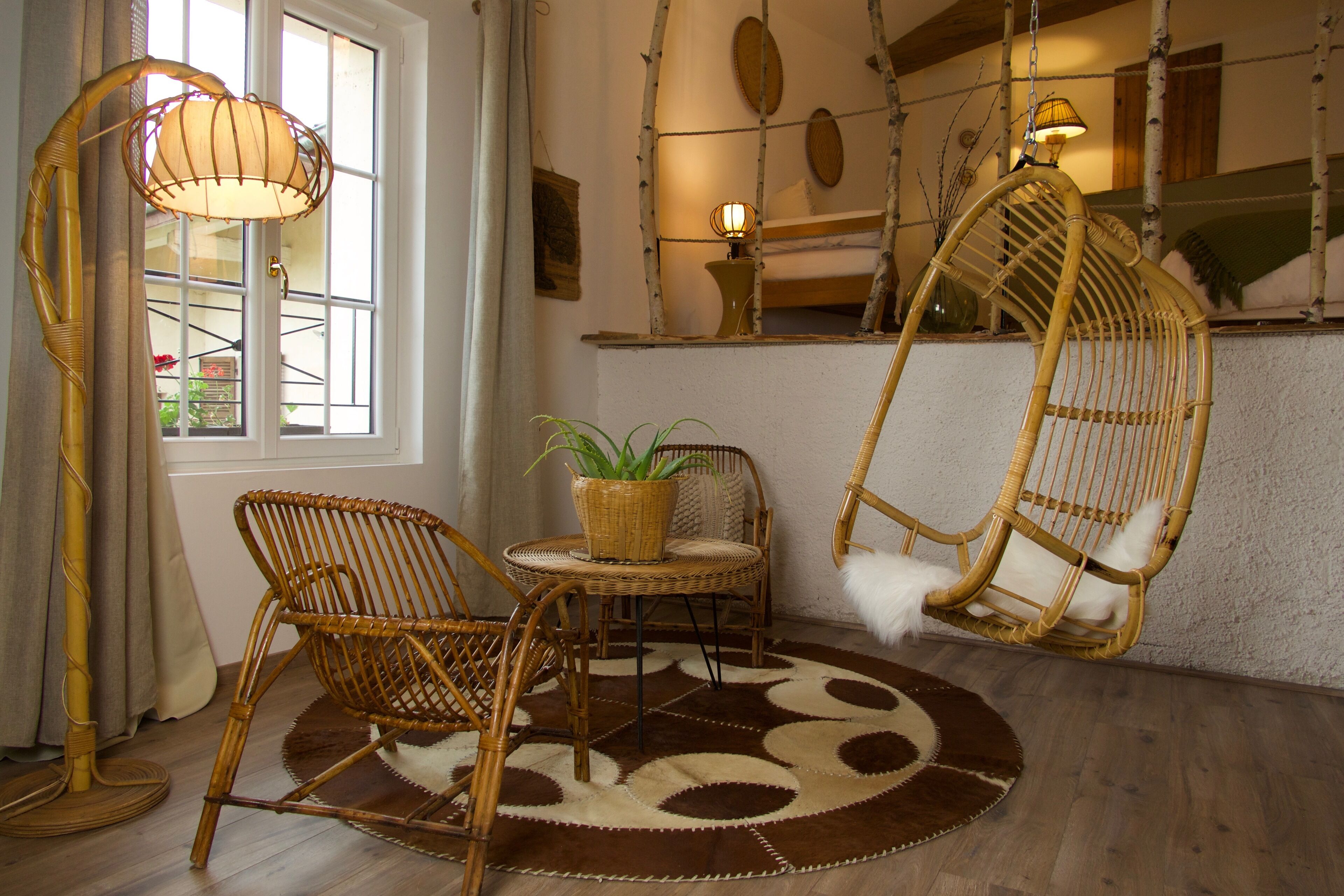 A room with a large window, a wicker chair, a hanging chair, and a floor lamp.