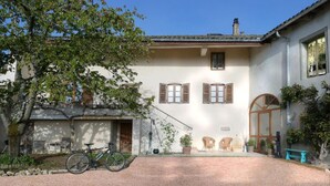 A two-story house with a covered patio, a bicycle, and potted plants. - Maison du Figuier (Lancie)