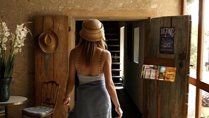 Una mujer caminando a través de una puerta de madera rústica hacia un cuarto con un sombrero en la pared y un letrero que dice "DEZING".