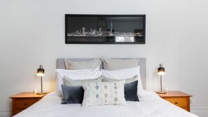En snyggt bäddad säng med utsikt över staden, två sänglampor och en inramad tavla ovanför sängen.