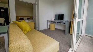 A modern hotel room with a sofa, a desk with a flat-screen TV, and a sliding glass door. - Cosy Renovated 1 Bedroom Apartment in CBD Hotel (Auckland)
