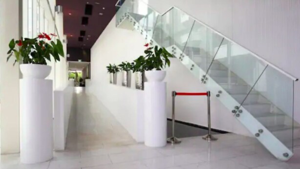 A modern interior with a glass staircase, white pillars, and potted plants. - Cosy Renovated 1 Bedroom Apartment in CBD Hotel (Auckland)