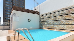 Une piscine sur le toit, agrémentée d’un panneau indiquant qu’il est interdit de plonger, d’un mur en pierre et offrant une vue sur le paysage urbain.