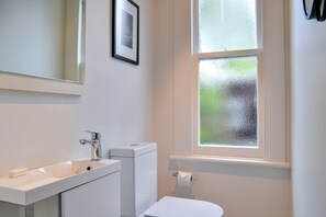 A bathroom with a white sink, toilet, and a window with frosted glass. - Heritage, Renovated 2 Bedroom Ponsonby Villa (Auckland)