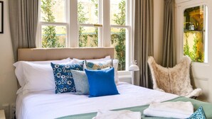 Un letto rifatto con cuscini decorati, una poltrona in pelliccia e vista su un paesaggio verdeggiante attraverso ampie finestre.
