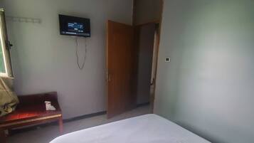 Una habitación con una cama, un televisor montado en la pared, una puerta de madera y un banco.