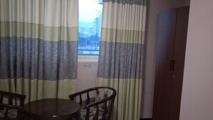 Una habitació amb taula de menjador i cadires, un armari i cortines.