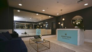 A modern living room with a sofa, coffee table, and a reception desk labeled 'HEREFORD RESIDENCES'. - 2 Bed Apt Heart of Ponsonby Gym (Auckland)