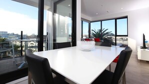 A modern dining area with a white table, black chairs, and a white bowl centerpiece. Large windows offer a view of the cityscape. - 2 Bed Apt Heart of Ponsonby Gym (Auckland)
