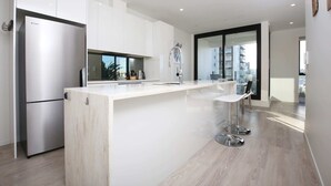 A modern kitchen with white cabinetry, a stainless steel refrigerator, a bar area with stools, and a large window providing a view of the city. - 2 Bed Apt Heart of Ponsonby Gym (Auckland)