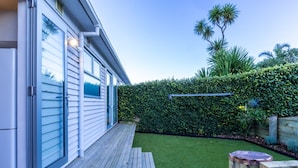A modern house with a wooden deck, a well-maintained lawn, and a dense hedge. - Sunny, Character 2 Bedroom Home - Mission Bay (Auckland)