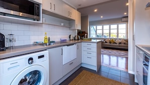 A modern kitchen with white cabinets, a built-in microwave, and a Samsung washing machine. - Sunny, Character 2 Bedroom Home - Mission Bay (Auckland)